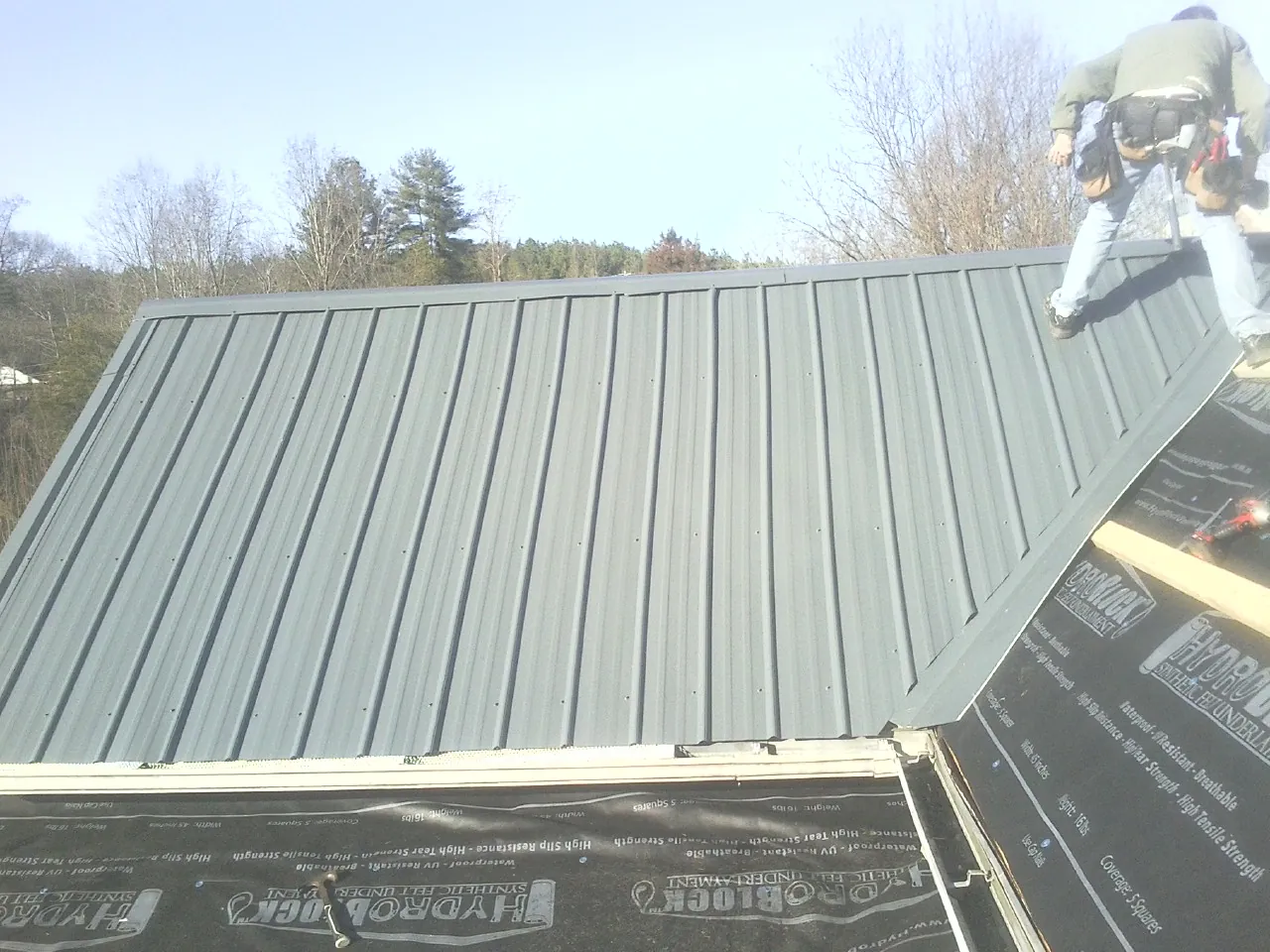 Crew installing dark green standing seam panels over synthetic underlayment in Sea Cliff