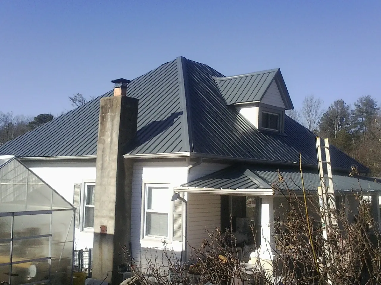 Dark blue standing seam metal roof on a white farmhouse with dormer — Slate & Tile Roof Repair by Roofing Brothers in Sea Cliff
