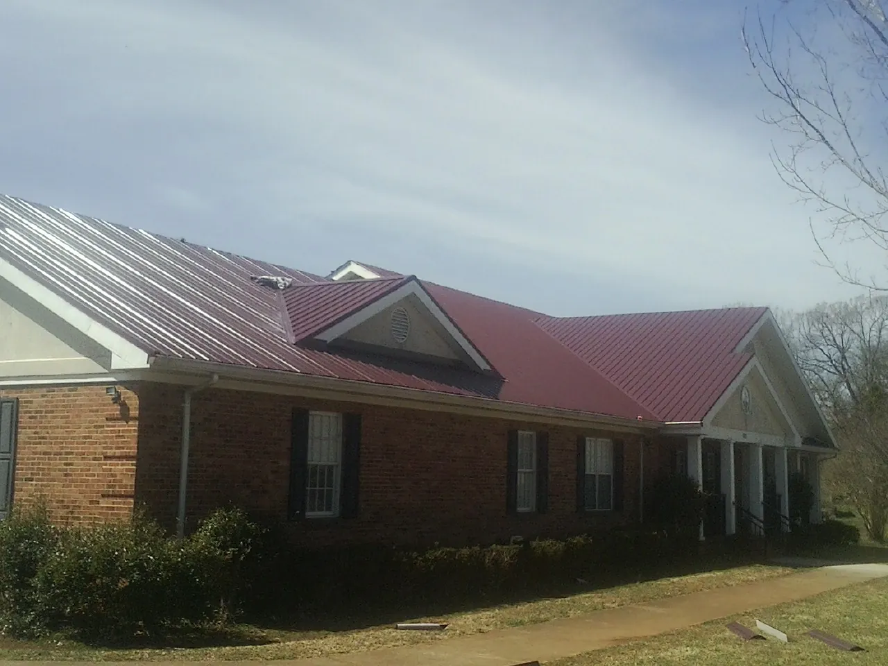 Red metal roof with gabled entries on a long brick building, from a Hail Damage Roof Repair job in Sea Cliff