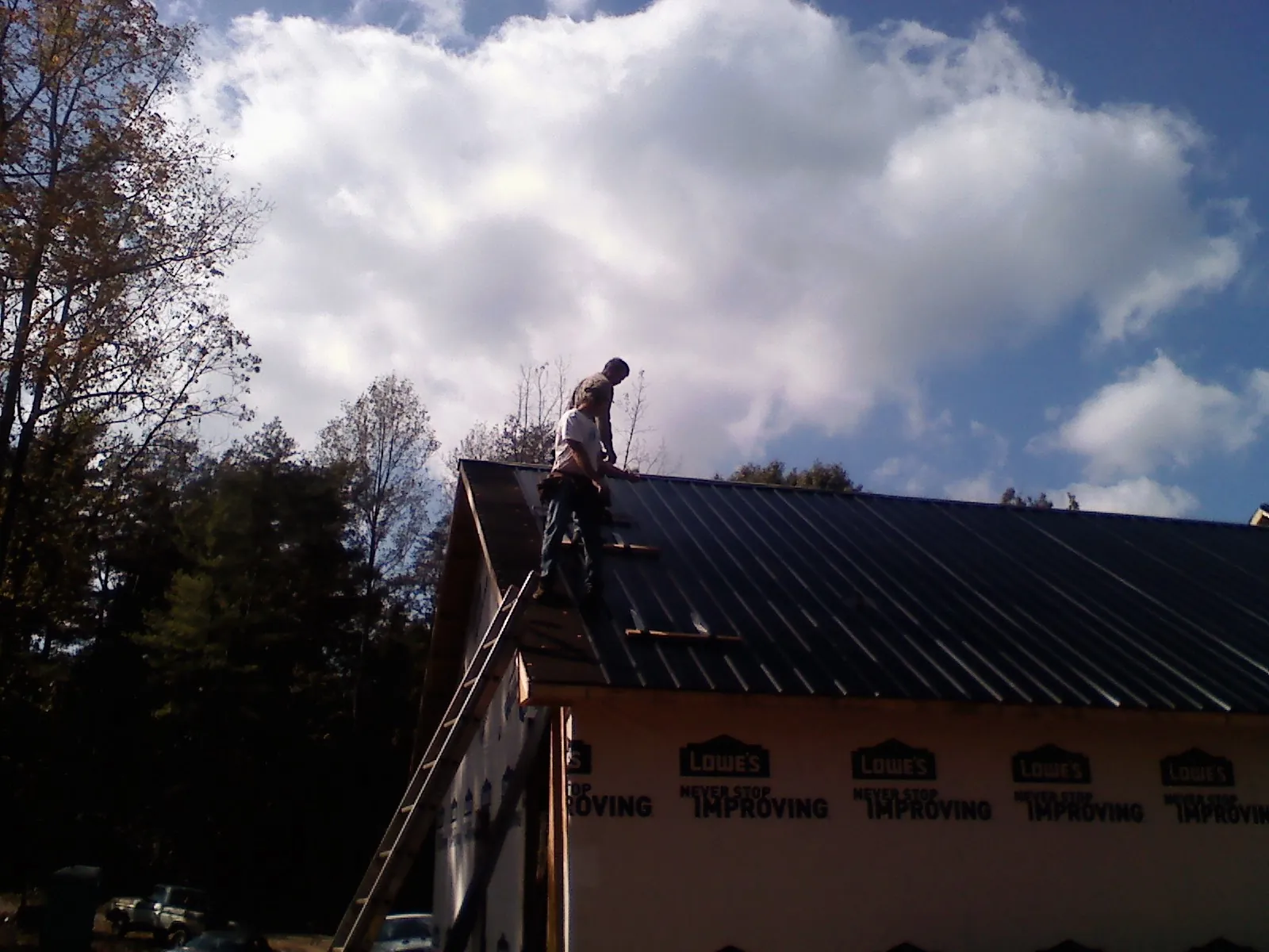 Roofer fastening dark metal panels high against a cloudy sky, from a Roof Inspection job in Sea Cliff