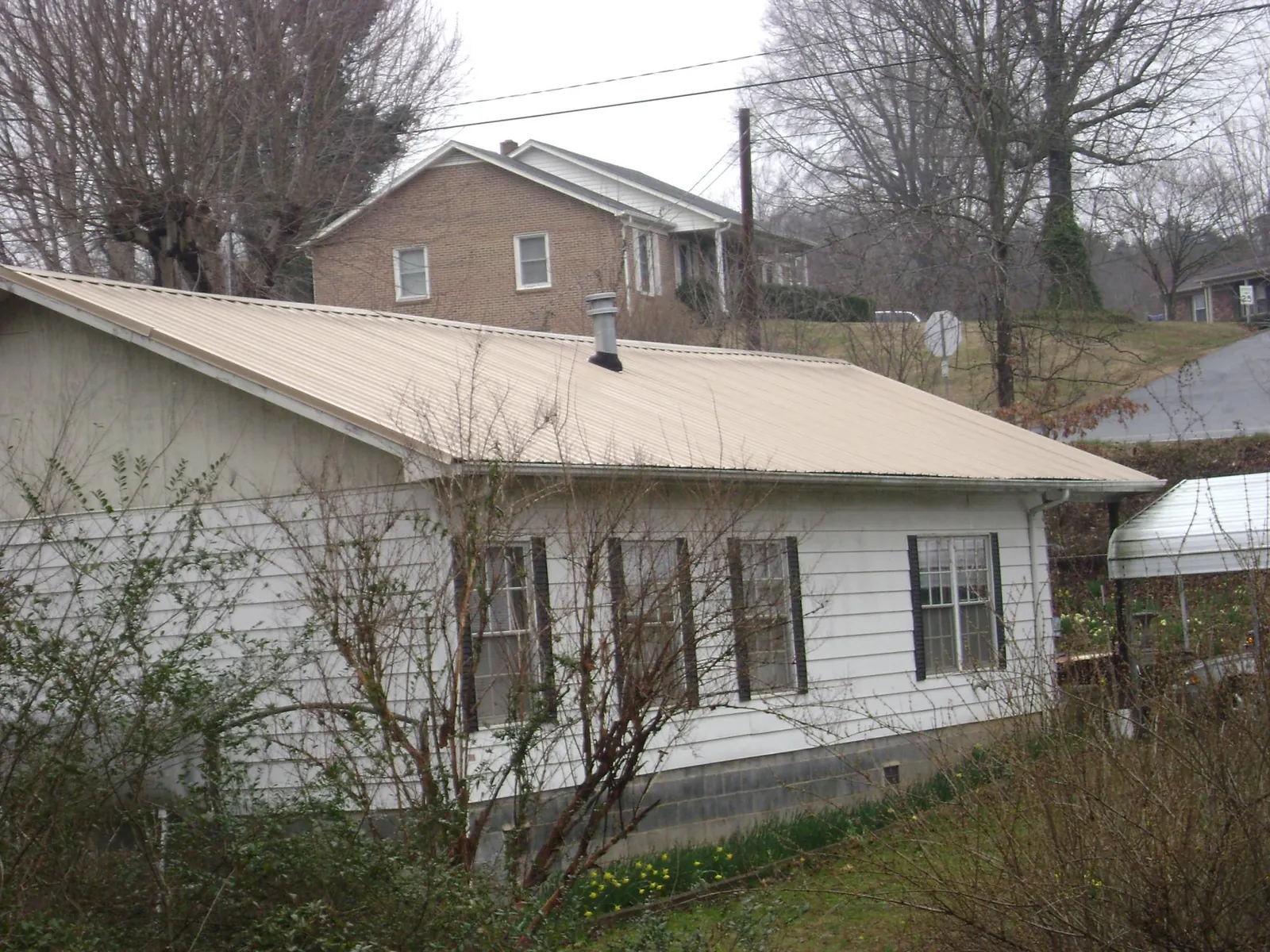 Tan metal roof on a white sided house set into a hillside — Commercial Roofing by Roofing Brothers in Sea Cliff